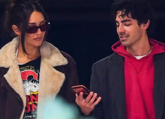 जो जोनस और उनकी प्रेमिका टाटियाना गैब्रिएला समुद्र तट पर हाथ में हाथ डाले खड़े, मुस्कुराते हुए