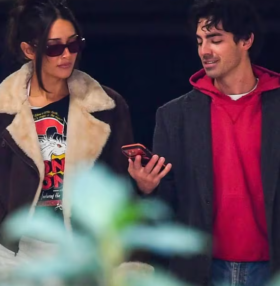 जो जोनस और उनकी प्रेमिका टाटियाना गैब्रिएला समुद्र तट पर हाथ में हाथ डाले खड़े, मुस्कुराते हुए