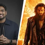 स्क्रीन अवार्ड्स 2026 के मंच पर मुस्कुराते हुए ज़किर खान, हाथ में माइक थामे हुए और बैकग्राउंड में 'धुरंधर 2' का पोस्टर