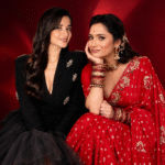 Two women posing together in stylish black and red outfits against a red backdrop.