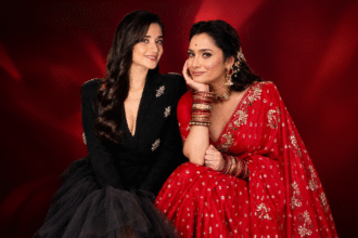 Two women posing together in stylish black and red outfits against a red backdrop.