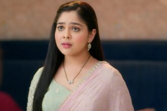 A woman wearing a pastel green blouse and pink saree, looking emotional and surprised indoors.