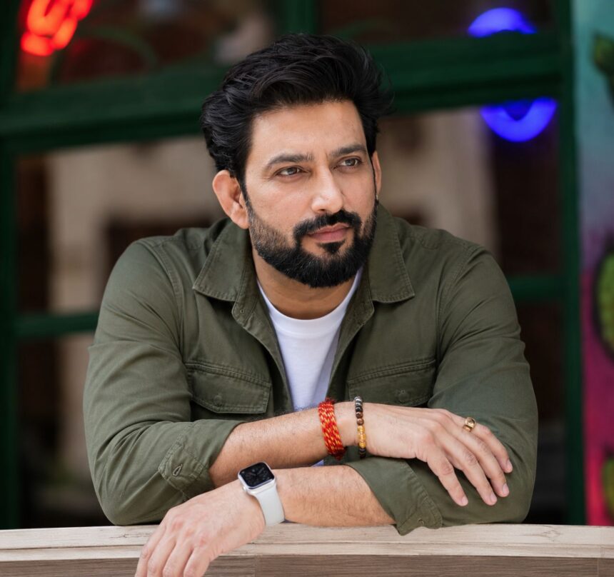 Bearded male celebrity in an olive green jacket posing for a photo