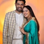 Smiling man and woman posing together, with the woman wearing a turquoise saree and the man in a checked blazer