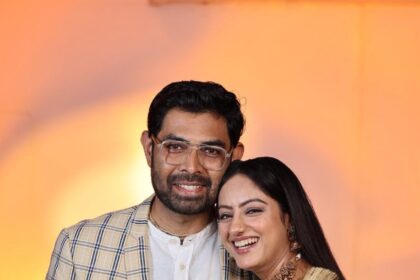 Smiling man and woman posing together, with the woman wearing a turquoise saree and the man in a checked blazer
