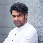 prabhas in a white outfit posting against a grey textured wall